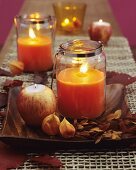 Orange candles in candle lanterns decorated with autumnal leaves and branches