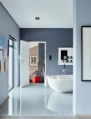 Glossy tiled floor and free-standing white bathtub in blue-grey bathroom