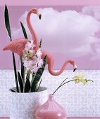 Plastic flamingos in potted house plant, pink vase and pink photo mural of clouds