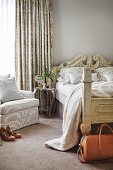 Antique wooden bed with carved headboard, delicate table and armchair in front of elegant curtain