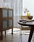 Dining table, wicker chair and sideboard with frosted glass door panels in interior in shades of brown