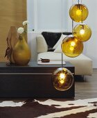 Goldfarbene Kugel-Hängeleuchte in Wohnraum mit Tierfellteppich, Ablagetisch und modernem Recamiere