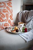 A cup of tea and mini biscuits and spicy canapés on a silver tray on an antique upholstered chair