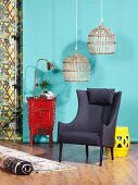 Wicker lampshades above grey armchair, Chinese cabinet and stool in front of turquoise wall