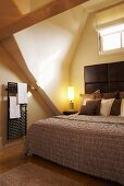 Double bed with headboard in attic niche with window and heated towel rail on wall