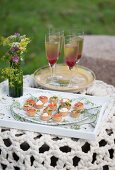 Verschiedene Canapés auf Schale und Sektcocktail in Stielgläsern auf Gartentisch