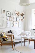 Fifties' armchair with wooden frame, set of coffee tables and sofa below pictures and antlers on wall