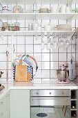 Küchenzeile übereck mit weisser Arbeitsplatte, darüber Regale mit Geschirr vor weisser Fliesenwand