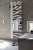 A white hand towel heater on a grey-tiled wall in a modern bathroom