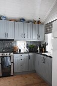 Rustic fitted kitchen with cabinets painted pale grey and white wood-clad walls