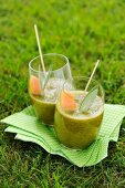 Two green smoothies garnished with melon on a napkin in a garden