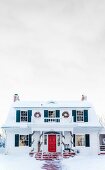 White, American country house with colourful shutters and Christmas decorations amongst snow