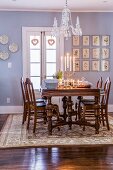 Crystal chandelier above lit candles on set dining table; botanical illustrations on lilac wall in background