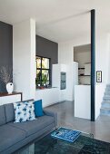 Offener Wohnraum mit grauem Sofa im Loungebereich, im Hintergrund Küche mit weissen Schrankoberflächen
