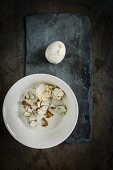 A peeled pickled egg with a linen patter on a slate surface with egg shell in a ceramic bowl on a wooden surface