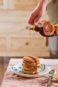 Maple syrup being poured onto a stack of pancakes