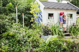 Two children outside play house in summery garden