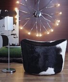 Kuhfell-Pouf und Designer-Stehaschenbecher vor Retro-Wandleuchte