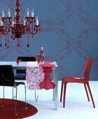 Roter Kronleuchter über Tisch mit gemusterten Tischläufern vor blauer Wand mit Ornamentmuster