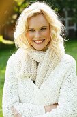 A young woman wearing a white, coarse-knit cardigan and scarf