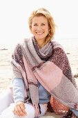 A blonde woman wearing a woollen shawl on a beach