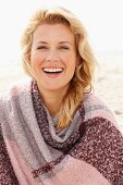 A blonde woman wearing a woollen shawl on a beach