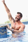 A dark-haired man with a beard cheering in a pool