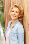 A blonde woman wearing a denim shirt leaning against a fence