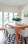 White armchairs around solid-wood table on black and white patterned rug in modern dining room