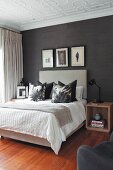 Scatter cushions arranged on double bed with tall, upholstered headboard against black wallpaper in elegant bedroom