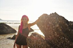 A blonde woman wearing a vest top standing on rocks by the sea