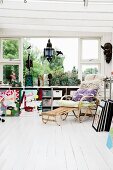 Cushions and fur rug on comfortable wicker lounger on white wooden floor in front of window with storage boxes on fitted shelving below sill