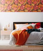Double bed with orange color accents, floral wallpaper over white base