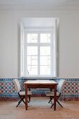 Table and upholstered chairs below window; dado strip covered with hand-painted tiles