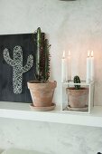Kaktustöpfe, Kerzenhalter und selbstgemachtes Fadenbild mit Kaktusmotiv auf schwarzem Grund