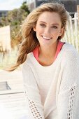 A young woman on a beach wearing a pink top and white knitted jumper