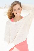 A young woman on a beach wearing a pink top and a white knitted jumper