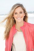 Junge Frau in hellem Shirt und lachsfarbener Lederjacke am Strand