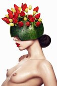 Topless woman wearing hat made from watermelon skin stuck with fruit skewers