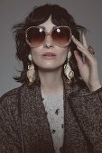 A dark haired woman wearing sunglasses and drop earrings