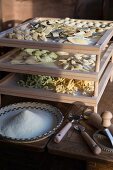 Fresh handmade pasta drying on a wooden rack with a bowl of cornmeal and pasta-making tools in the forground