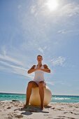 A woman on a beach practising yoga with an exercise ball