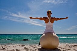A woman practising yoga on a beach with an exercise ball