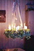 A hanging Advent wreath made from green twigs and pine spigs with white pillar candles