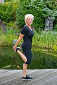 Blonde Frau in sportlicher Bekleidung macht Dehnübung auf dem Steg
