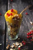 Mango sorbet with redcurrants and wafer crumbs in a glass on a wooden table