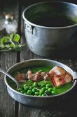 Cream of pea soup with fried bacon on a wooden table