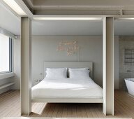 Blick zwischen heller Stahlträgerkonstruktion auf Doppelbett mit weisser Bettwäsche und beleuchtetem Schriftzug an hellgrauer Wand