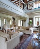Pale sofa set on Oriental rug in living area below gallery in renovated country house with white-painted wood-beamed ceiling