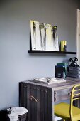 Wooden desk and yellow chair against dark gray wall, black shelf console with modern picture